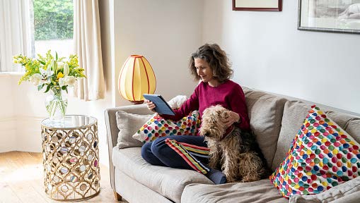 Woman sitting comfortably on a couch with her dog while reading from her iPad