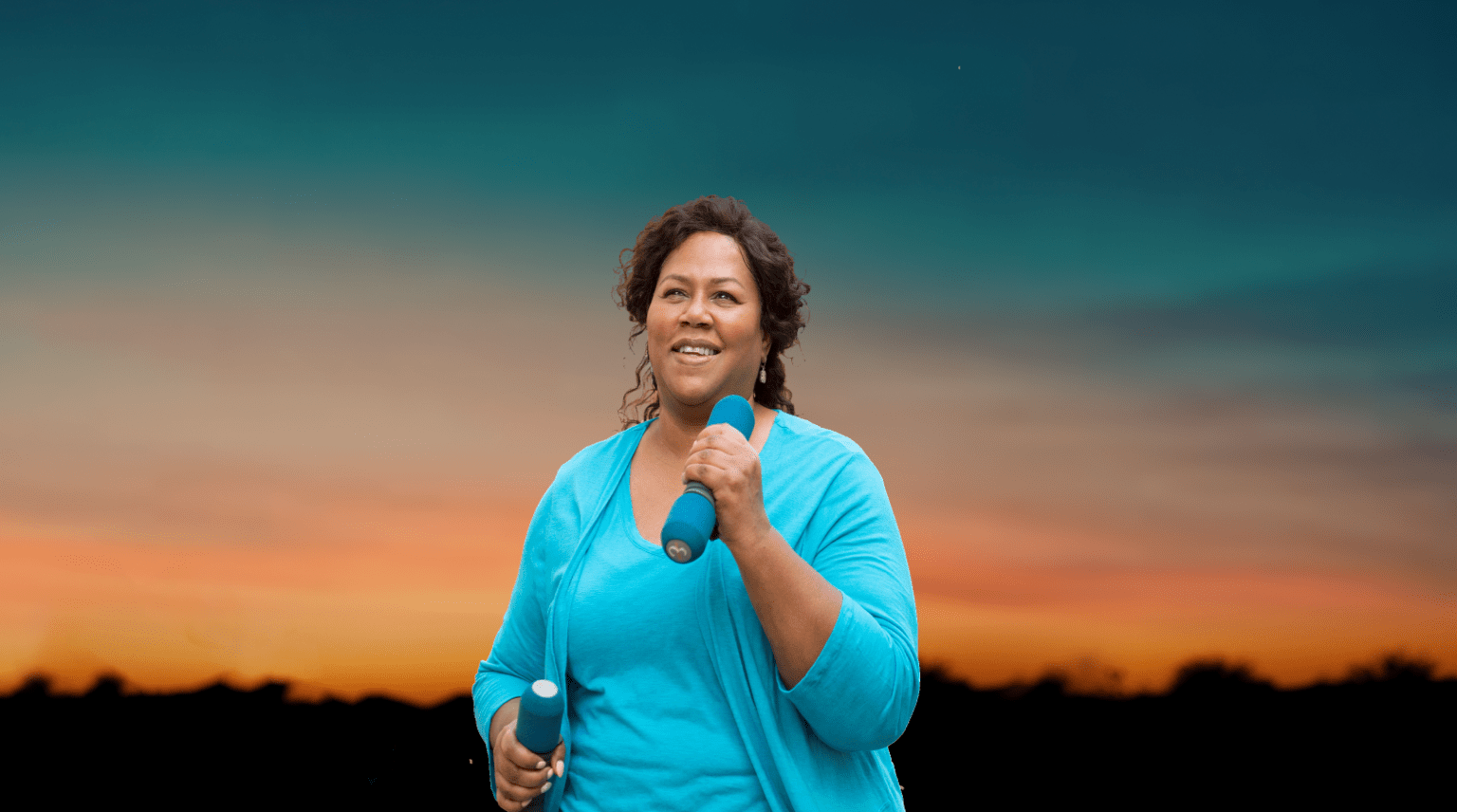 Banner image of a middle-aged woman enthusiastically walking outdoors with a pair of light weights in her hands 